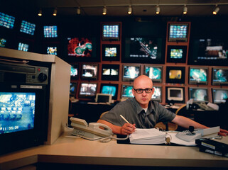 Man sitting at desk surrounded by security videos in a control room