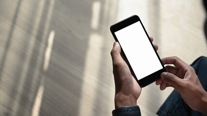 Close up view of man hands holding smart phone with white screen while sitting on wooden floor.
