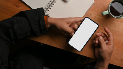 Top view of male hands using smartphone on wooden worktable