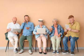 Senior people with different devices sitting on chairs in room