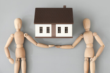 Wooden mannequins and house model on grey background