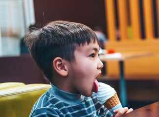 happy little boy eating white ice cream in a cone in a cafe restaurant during lunch. the concept of childhood and happiness