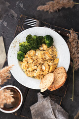 Scrambled eggs in a white plate. Scrambled eggs and broccoli. Healthy breakfast or lunch. Top view. Dark background. Vertical view