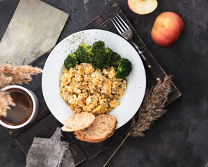Scrambled eggs in a white plate. Scrambled eggs and broccoli. Healthy breakfast or lunch. Top view. Dark background
