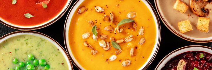 Vegan soup panorama. An assortment of vegetable soups, shot from the top on a black background