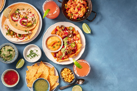 Mexican Food, An Overhead Flat Lay. Nachos, Tacos, And Other Snacks On A Blue Background With Copy Space