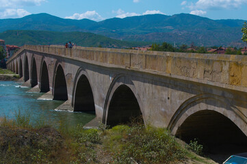 Fototapeta na wymiar Historical Ottoman stone bridge and Kızılırmak. River and bridge view. Rural settlement and arched structure. 