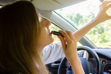 Woman is applying makeup in the car. Girl with lipstick behind the wheel. Dangerous situation on...