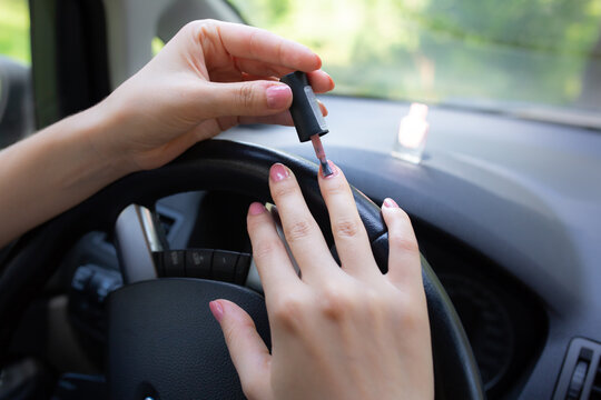 Woman is making manicure in the car. Girl applying  nail polish behind the wheel. Dangerous situation on the road.