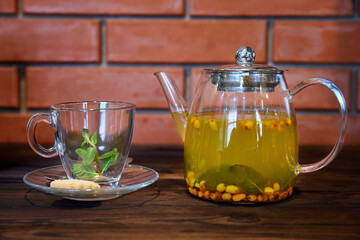 Sea buckthorn and mint tea in a transparent glass teapot. Close-up, selective focus