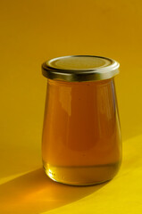 Natural sugar substitute, healthy food concept. Raw bee honey in glass jar on yellow background.
