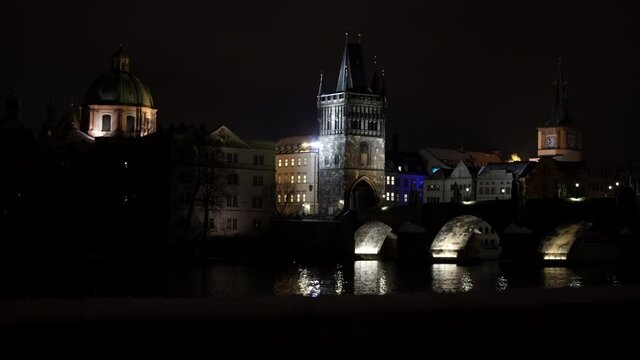 refocus in to Charles Bridge and old bridge tower on the Vltava river in the center of Prague through the silhouettes of branches at night in winter