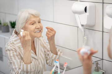 Gray-haired woman cleaning her teeth and using floss