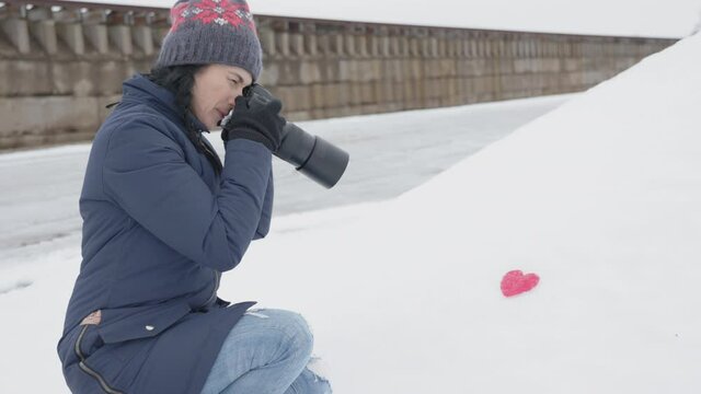Woman photographer take picture of paper heart on snow

