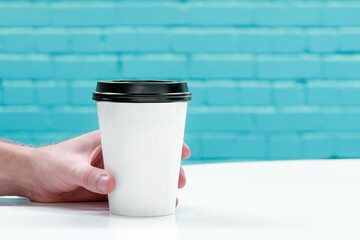 Close up of hand holding take away coffee. Brick wall background with copy space for text