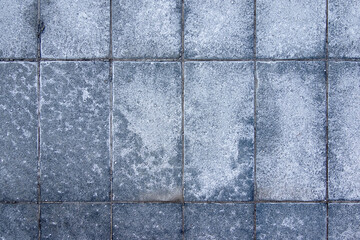 Salt spread on icy pavement in the city. Bricks covered with salt stains. Slippery sidewalk in winter.