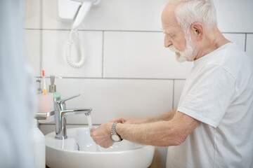 Gray-haired man in white tshirt washing up in the bathroom
