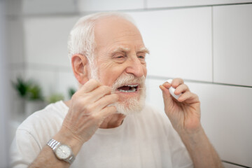 Gray-haired man in white tshirt cleaning teeth with a floss