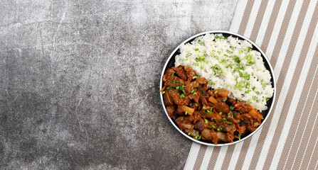 Stewed chicken gizzards with boiled rice on a round plate on a dark gray background. Top view, flat lay