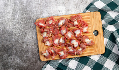 Raw chicken gizzards on a rectangular cutting wooden board on a dark grey background. Top view, flat lay