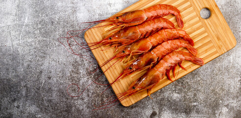 Argentinian raw red prawns (shrimps) with heads on a rectangular cutting wooden board on a dark grey background. Top view, flat lay
