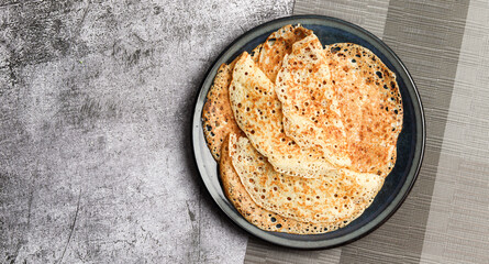 Traditional russian yeast thin pancakes (crepes) on a round plate on a dark gray background. Top view, flat lay