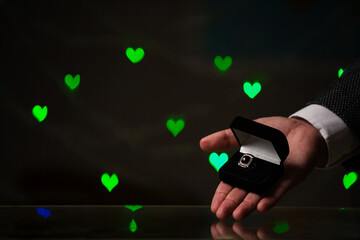 Hand holds black box with ring on background of hearts