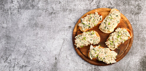 Tuna Salad open faced Sandwiches on a round wooden cutting board on a dark grey background. Top view, flat lay