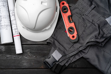 Construction worker unifrom, hardhat and blueprints on wooden background