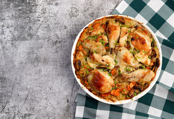 Oven Baked Chicken and Rice with onions, carrots and herbs in a white baking dish on a dark grey background. Top view, flat lay