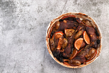 Roasted duck legs in a white baking dish on a dark background. Top view, flat lay