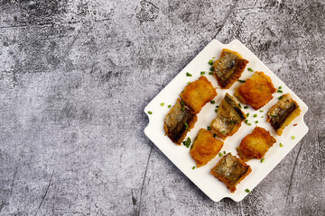Fried Pollock fish fillet on a white square plate on a dark background. Top view, flat lay.