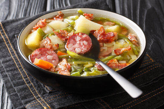 Luxembourgish soup of green beans, potatoes, leeks, carrots with the addition of sausages and bacon close-up in a plate on the table. Horizontal