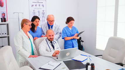 Fototapeta na wymiar Concentrated medical team using laptop together in the hospital meeting room consulting with mentor physician. Clinic expert therapist talking with colleagues about disease, medicine professional