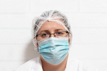 Close up of tired exhausted desperate caucasian female doctor in protective uniform and mask. After long shift at clinic doctor leaned against the wall to rest for a while. Fighting coronavirus. 