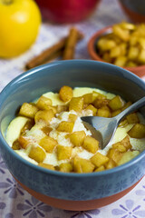 A spoon taking semolina pudding with caramelized apple cubes from a bowl