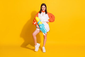 Fototapeta na wymiar Full length photo portrait of woman holding water gun in one hand isolated on vivid yellow colored background