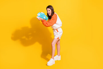 Photo portrait full body view of playful excited woman shooting water gun isolated on vivid yellow colored background