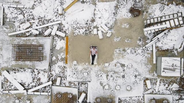 Aerial view on top builder who took a break from construction at Zik. The man drinks juice and relaxes on the construction of the foundation of the house. The camera flies away from the man uphill.