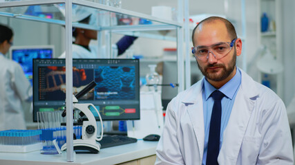 Naklejka premium Portrait of exhausted chemist looking at camera in modern equipped lab. Multiethnic team examining virus evolution using high tech and chemistry tools for scientific research, vaccine development.