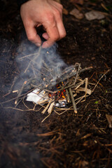 A man kindles a fire in the forest on vacation. Close-up male hand in the process of kindling a fire at a picnic in the forest