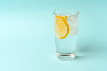 A glass of water with ice and lemon on a light blue background, the concept of a healthy lifestyle