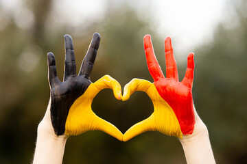 Kid hands painted in Belgium flag color show symbol of heart and love gesture on nature background