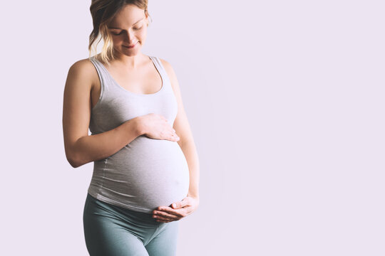 Beautiful young pregnant woman in good fit holds hands on her belly. Happy mother waiting for baby birth during pregnancy. - Powered by Adobe