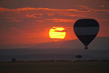 Sunset, hot air balloon silhouette, meadows and mountains. Large numbers of animals migrate to the Masai Mara National Wildlife Refuge in Kenya, Africa. 2016.