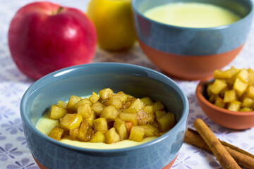 Semolina pudding in a bowl with caramelized apple cubes with apples and cinnamon in background