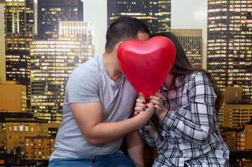 A girl and a guy kiss, covered with a balloon in the form of a heart, holding it in their hands. Valentine's Day.