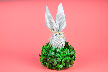 Happy easter. DIY egg with bunny ears on a pink background. hide easter eggs in the grass