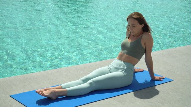 Young fitness woman in sportwear practicing yoga by swimming pool in Morning outdoors at sport club . sport girl doing exercise . workout healthy lifestyle . training. stretching