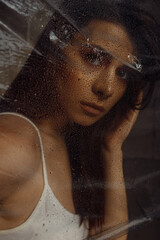 Photo portrait of pretty brunette woman with make up touching transparent cellophane covered with water drops 